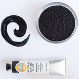 A top down view of the Natural earth paint in black ochre next to a bowl of black pigment and a paint streak showing the consistency. 