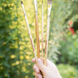 A adult hand holding 4 Natural Earth Paint eco paint brushes 