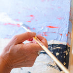A adult hand holding a Natural Earth paint eco paint brush painting on a painted canvas 