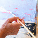 A adult hand holding a Natural Earth paint eco paint brush painting on a painted canvas 