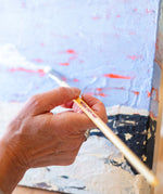 A adult hand holding a Natural Earth paint eco paint brush painting on a painted canvas 