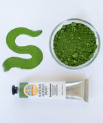 A top down view of the Natural earth paint tube in emerald green next to a bowl of matching paint pigment and a streak showing the consistency. 