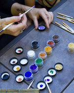 Close up of some hands painting with the Natural Earth kids coloured face paint jars on a grey table