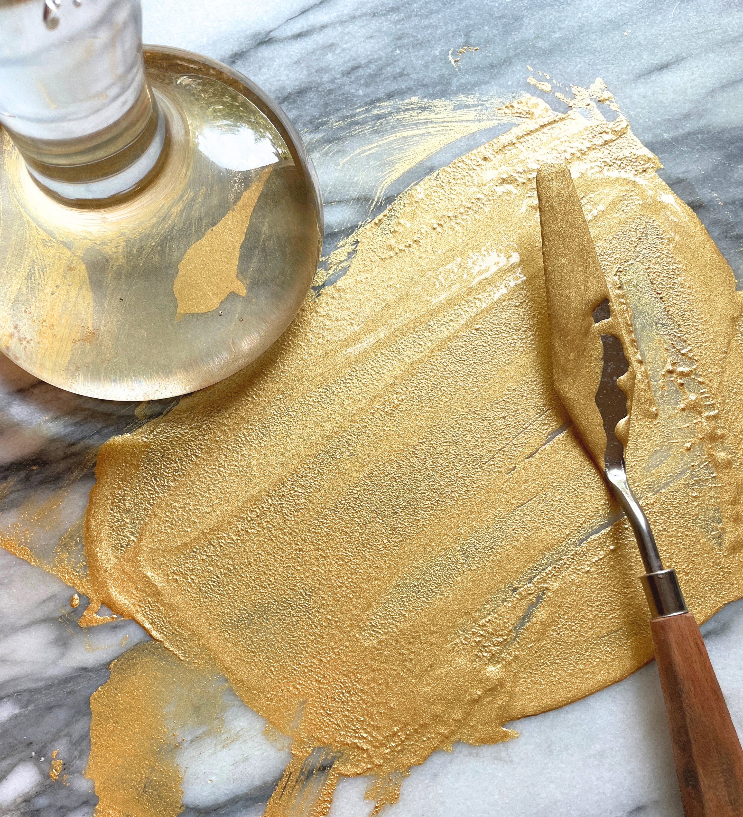 Natural Earth Paint palette knife with wooden handle spreading gold glittery paint on a stone surface. 