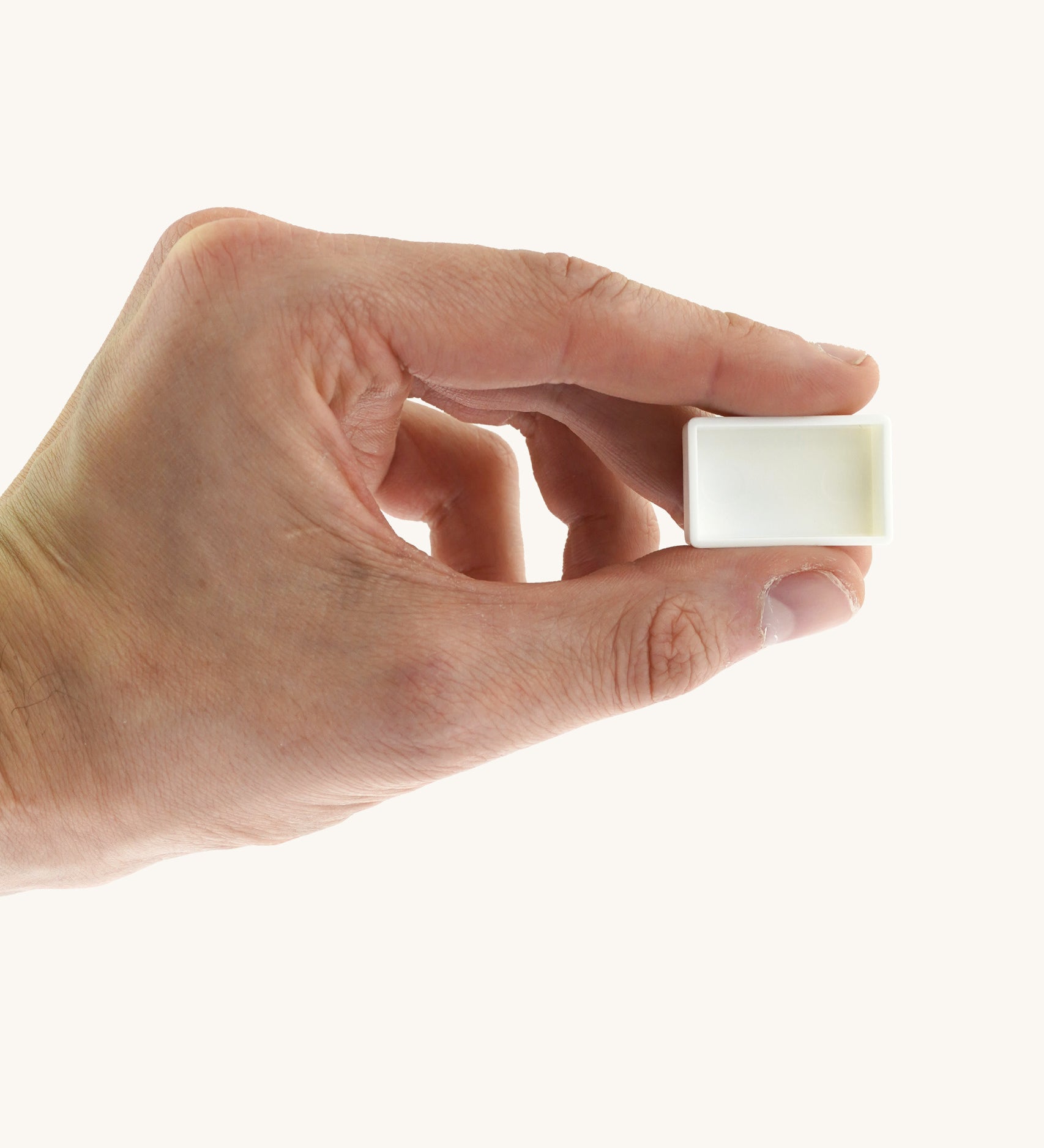 An adult hand holding the white blank watercolour paint pan from Natural Earth Paint  for size reference. 
