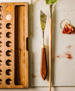 A top down view of the Natural Earth paint watercolour wooden palette with brush holder next to a palette knife and brush 