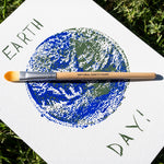 A painting of the earth with the words earth day written around it. The paint brush from the The Natural Earth Paint Petite Paint Kit has been placed on the painting. 