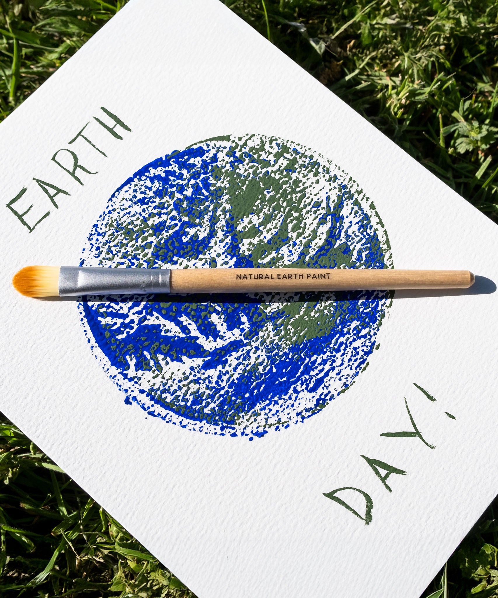 A painting of the earth with the words earth day written around it. The paint brush from the The Natural Earth Paint Petite Paint Kit has been placed on the painting. 