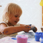 A close up of a child mixing different coloured Neogrun crystal finger paints on a table. 