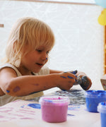 A close up of a child mixing different coloured Neogrun crystal finger paints on a table. 