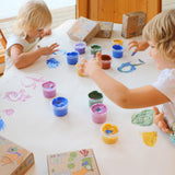 A top down view of 2 kids being creative using the Neogrun crystal finger paints on a white table cloth.