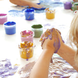 A close up of a child's hand with the gold and purple Neogrun crystal finger paint mixed together showing the consistency of the paint