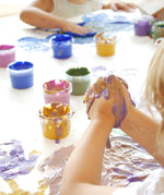 A close up of a child's hand with the gold and purple Neogrun crystal finger paint mixed together showing the consistency of the paint
