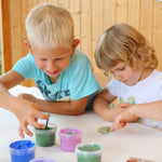 Two kids with their fingers in the Neogrun finger paint in the crystal colour set. showing 2 kids being creative. Features a pink, green blue and purple coloured paint. 