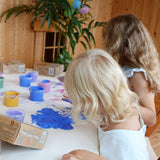 2 kids painting on a white cloth with their finger using the Neogrun blue, purple and gold crystal finger paint