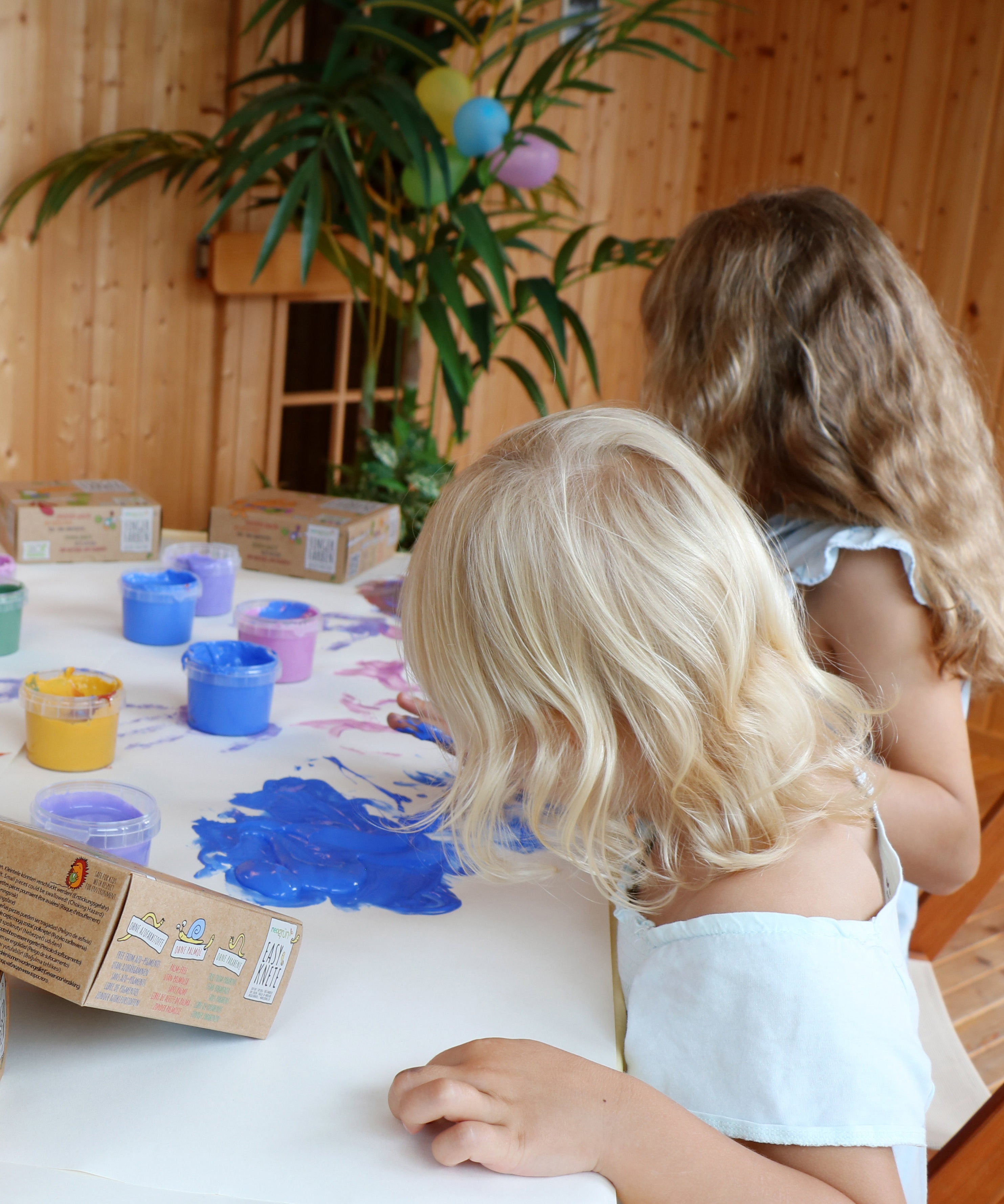 2 kids painting on a white cloth with their finger using the Neogrun blue, purple and gold crystal finger paint