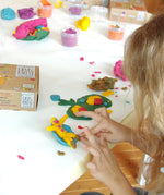 A top down view of a child being creative with the Neogrun organic play dough showing a little figure on a seat next to flowers.