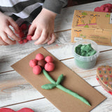 A close up of a child's hands forming balls of dough with the pink coloured neogrun organic play dough. They have created a flower with the play dough and placed it on a piece of cardboard. 