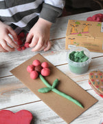 A close up of a child's hands forming balls of dough with the pink coloured neogrun organic play dough. They have created a flower with the play dough and placed it on a piece of cardboard. 