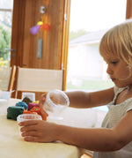 A child holding the plastic tub that hold the Neogrun play dough showing the size of the tubs.