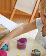 A child rolling  the blue and pink Neogrun play dough with the purple and green play dough in plastic tubs showing the consistency and texture of the clay