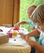 2 kids sitting. by the table and rolling the different coloured Neogrun organic play dough