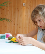 A child sitting beside a table playing with the Neogrun organic play dough on a white table cloth