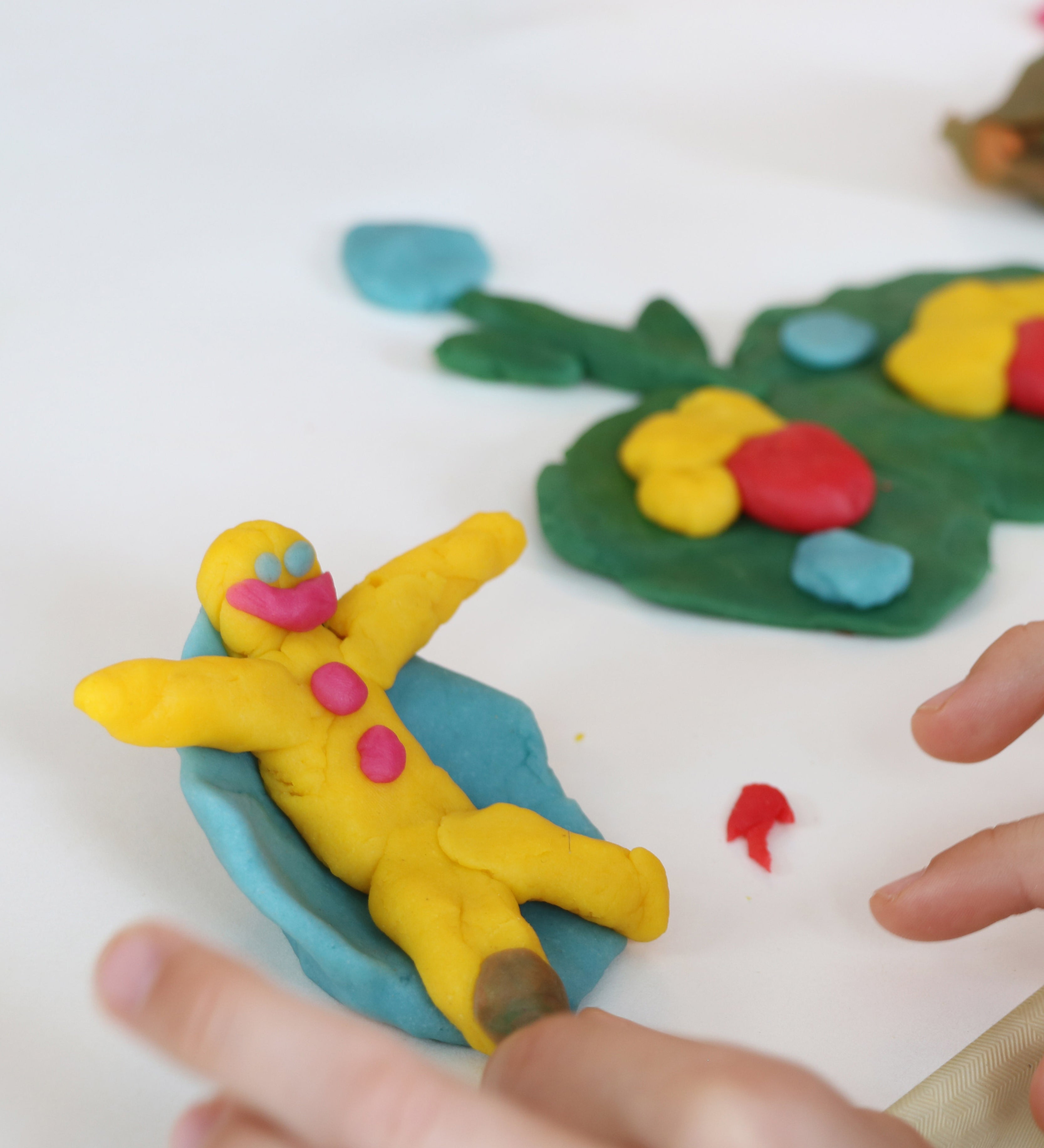 A close up of a child's hand being creative and moulded the Neogrun organic play dough into a little figure on a blue seat. 