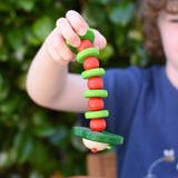 Nic apple worm baby wooden grasping toy in a child's hand. Smiling worm on a flexible rope lined with chunky red and green beads.