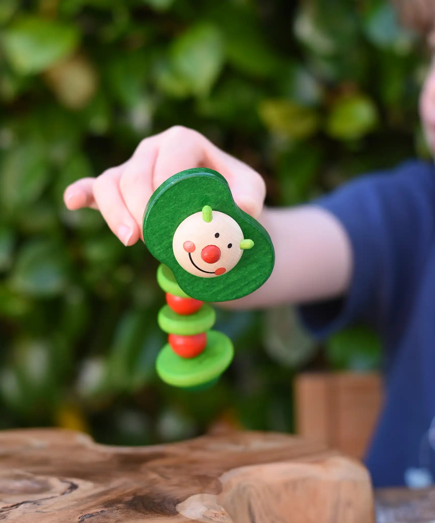 Nic apple worm baby wooden grasping toy in a child's hand. Smiling worm on a flexible rope lined with chunky red and green beads. 