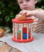 Child playing with the Nic BIO red rolling shape sorter wooden toy with 6 wooden blocks.