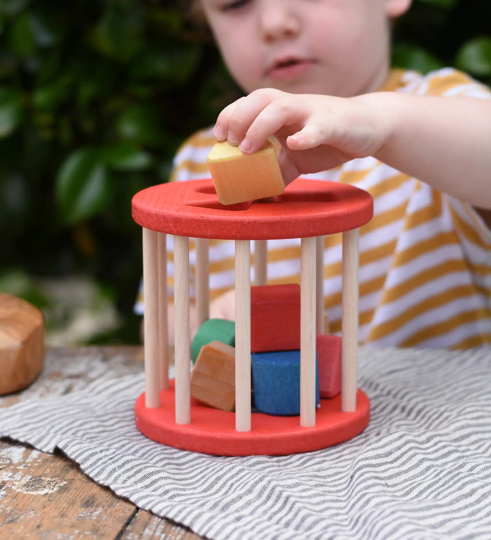 Child playing with the Nic BIO red rolling shape sorter wooden toy with 6 wooden blocks.