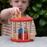 Child playing with the Nic BIO red rolling shape sorter wooden toy with 6 wooden blocks.