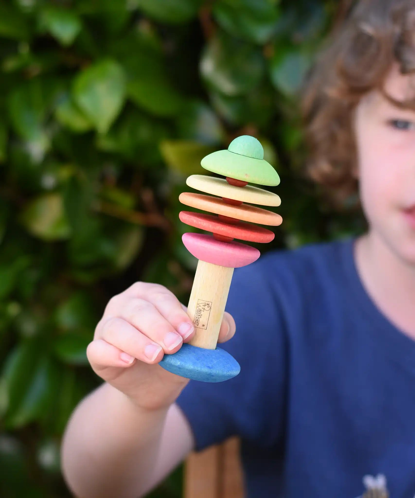 Child holding the Nic Toys bio wooden rattling tree baby toy. Coloured disks for making a noise and a wooden handle for grip.