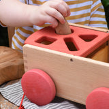 Child posting a Graapt Nin through the circle slot in the Nic wooden carriage shape sorter pull along toy. 