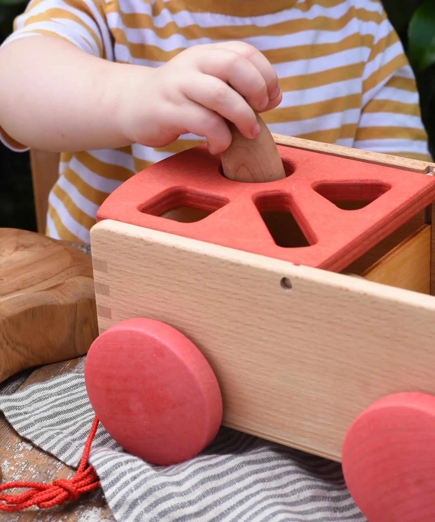 Child posting a Graapt Nin through the circle slot in the Nic wooden carriage shape sorter pull along toy. 