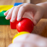 A close up of a child's hand placing a red coloured wooden ball on a Nic Cubio ball run track.