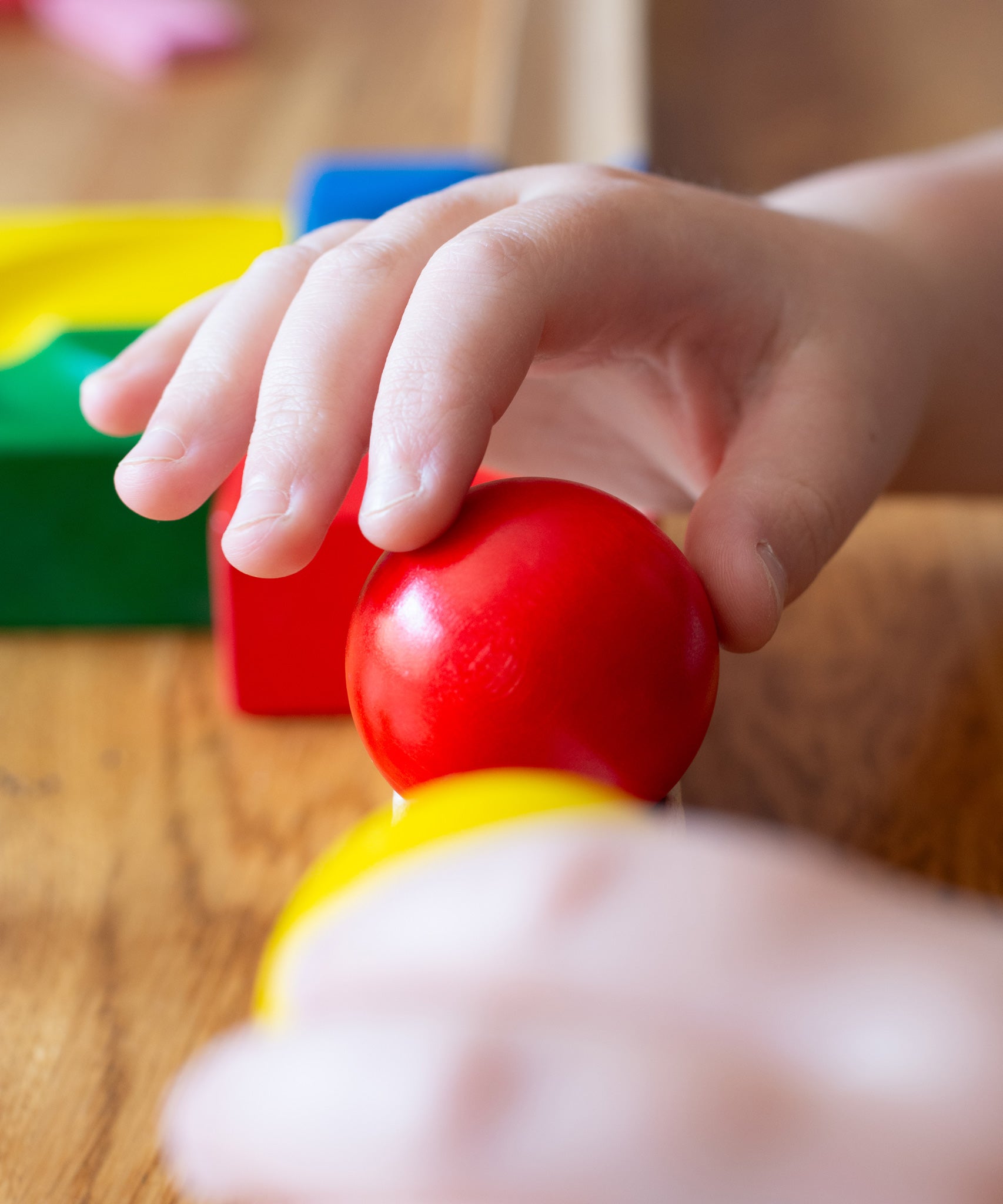 A close up of a child's hand placing a red coloured wooden ball on a Nic Cubio ball run track.