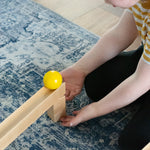A child placing a yellow coloured ball on the track set up using pieces from the Nic Cubio wooden Ball Track Extension Set.
