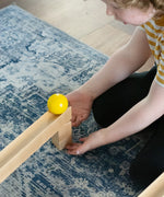 A child placing a yellow coloured ball on the track set up using pieces from the Nic Cubio wooden Ball Track Extension Set.