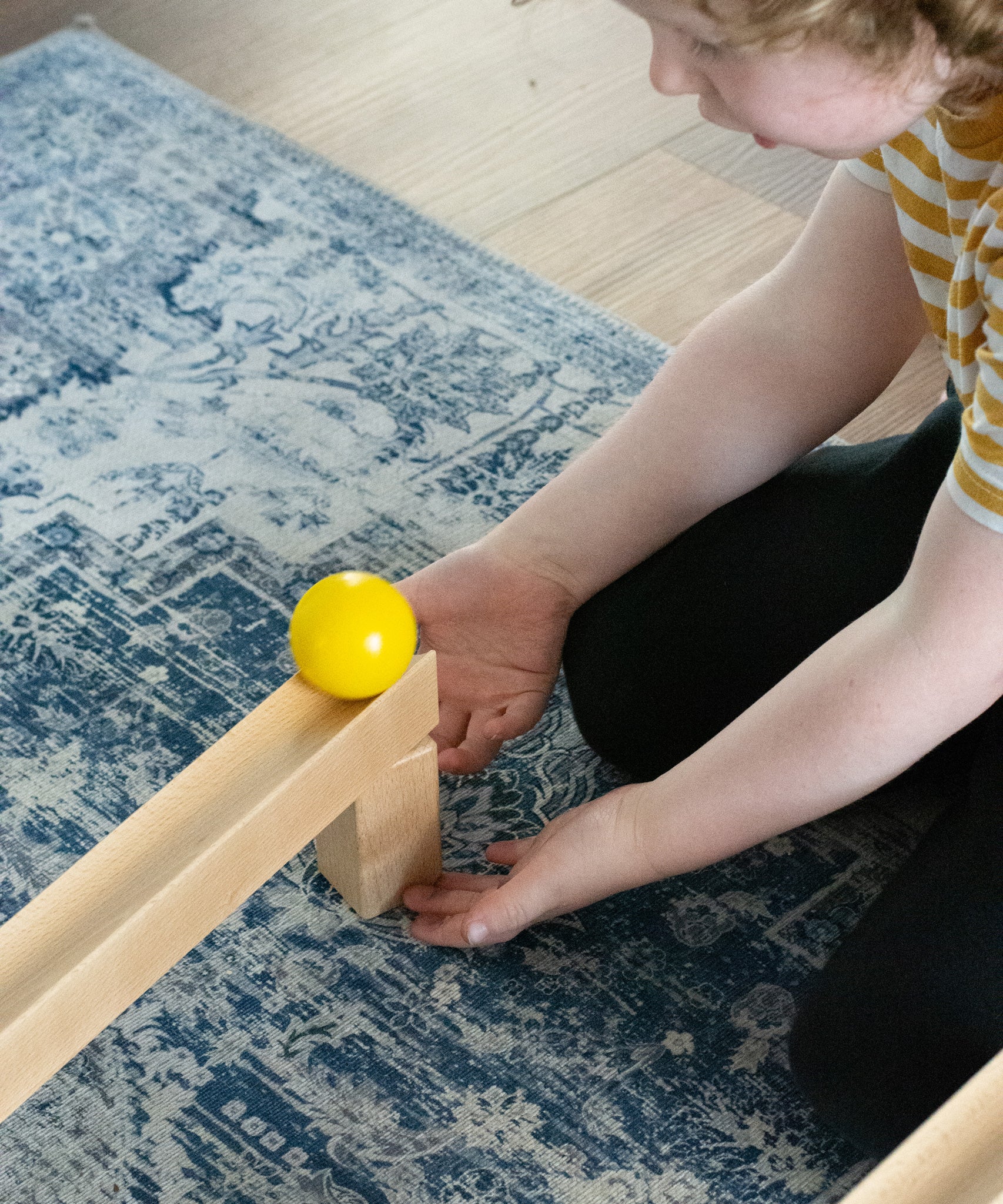 A child placing a yellow coloured ball on the track set up using pieces from the Nic Cubio wooden Ball Track Extension Set.