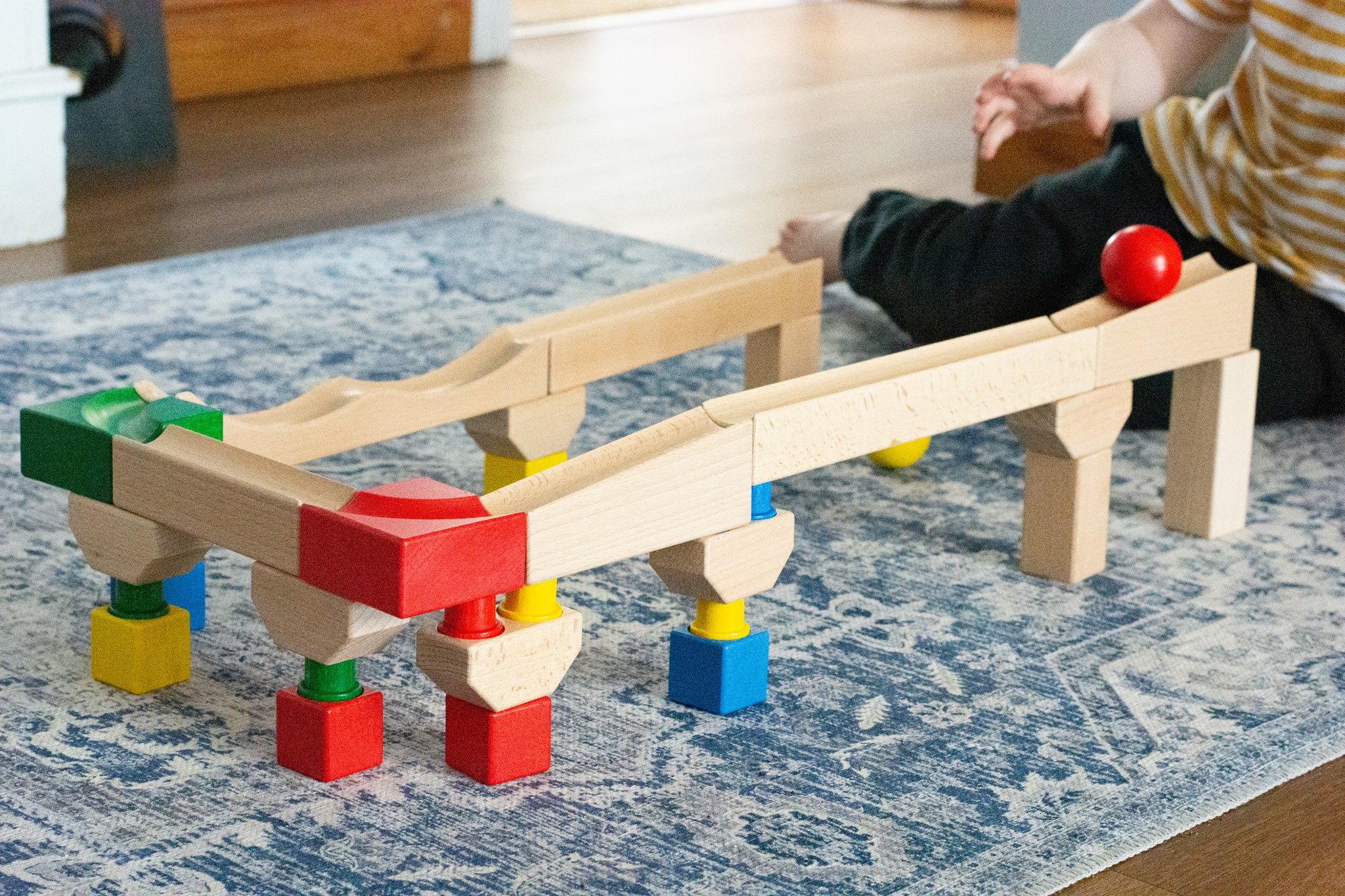 Nic Cubio wooden Ball Track Extension Set shown set up, a child has just placed a red ball on the track. Wooden balls are available to purchase separately. 