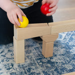 A close up of a child placing a yellow wooden ball on a piece of track from the Nic Cubio wooden Ball Track Extension Set.