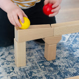 A close up of a child placing a yellow wooden ball on a piece of track from the Nic Cubio wooden Ball Track Extension Set.