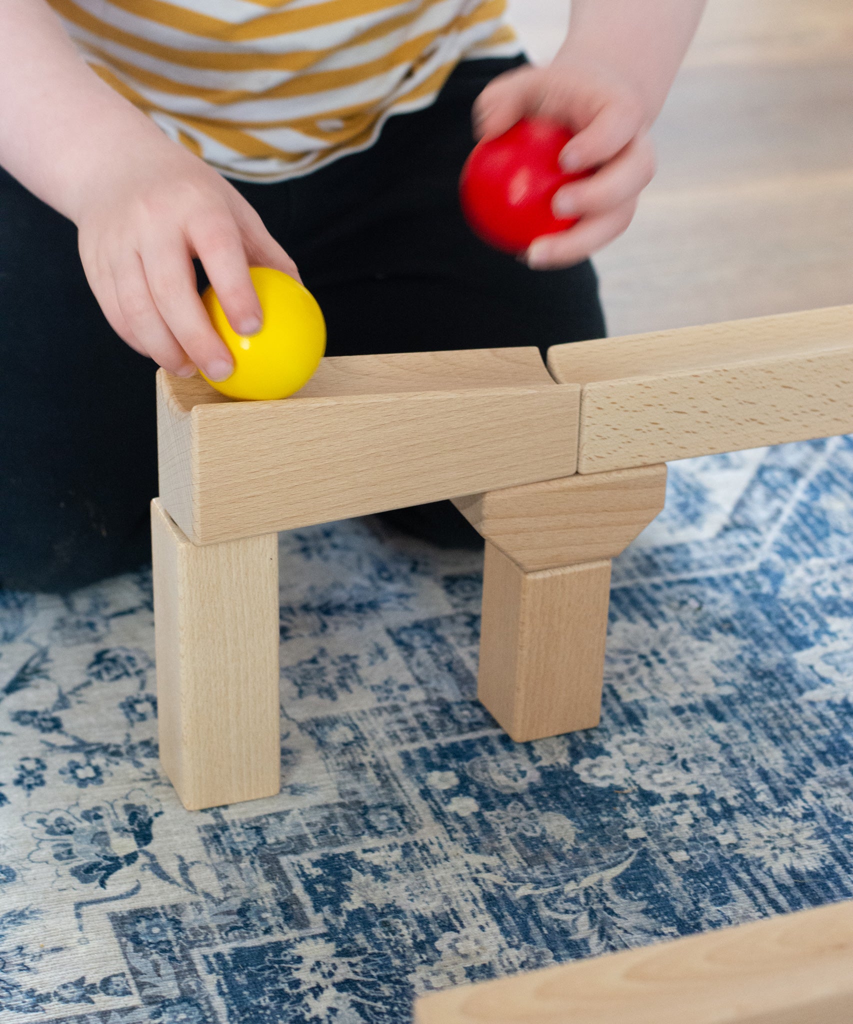 A close up of a child placing a yellow wooden ball on a piece of track from the Nic Cubio wooden Ball Track Extension Set.