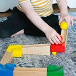 A child playing with the Nic Cubio Wooden Marble Run Starter Set. The child can be seen placing the red and yellow coloured wooden ball on to the track.