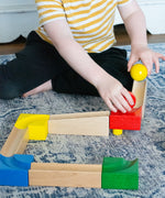 A child playing with the Nic Cubio Wooden Marble Run Starter Set. The child can be seen placing the red and yellow coloured wooden ball on to the track.