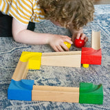 A child kneeling down next to the Nic Cubio Wooden Marble Run Starter Set.