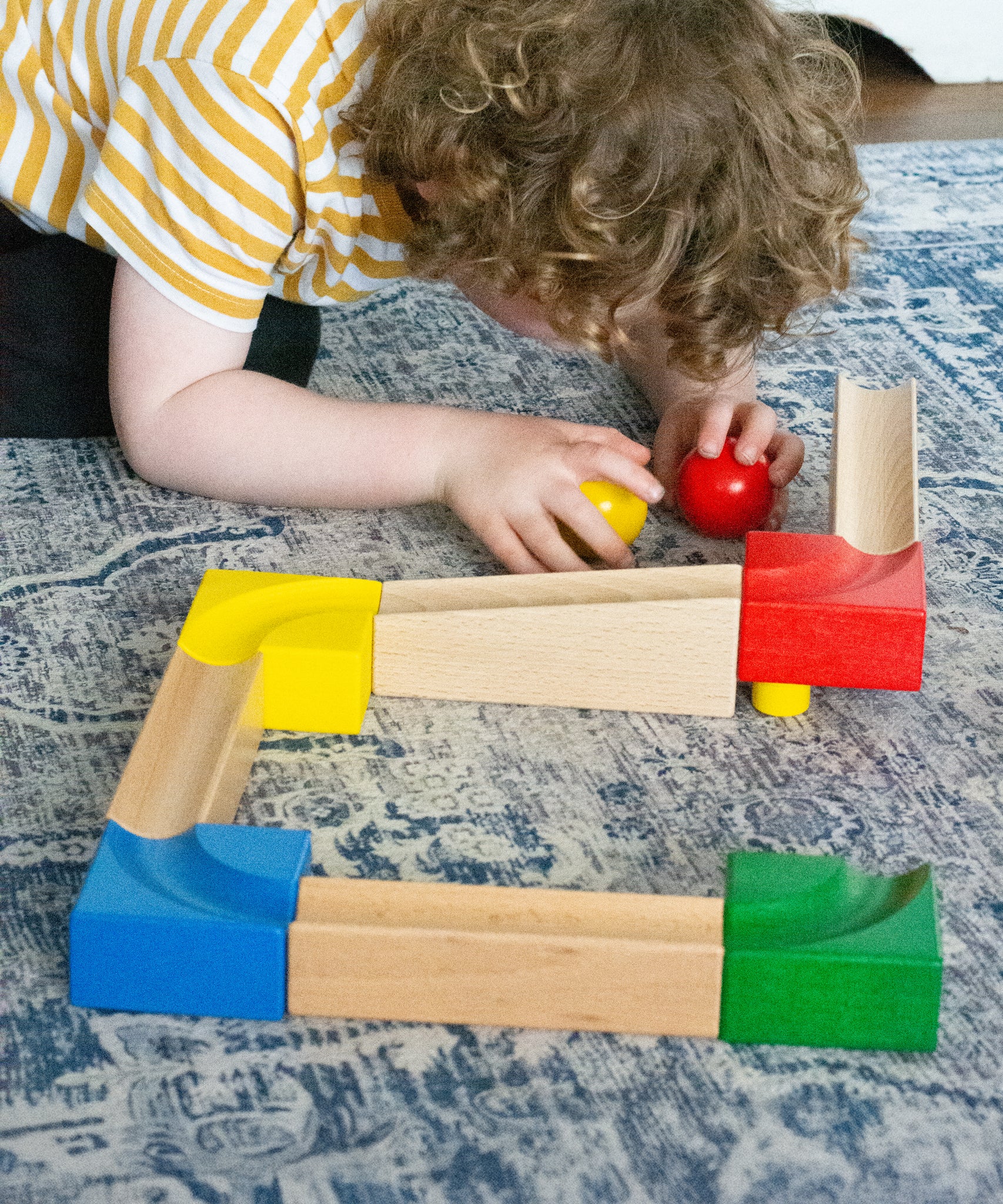 A child kneeling down next to the Nic Cubio Wooden Marble Run Starter Set.