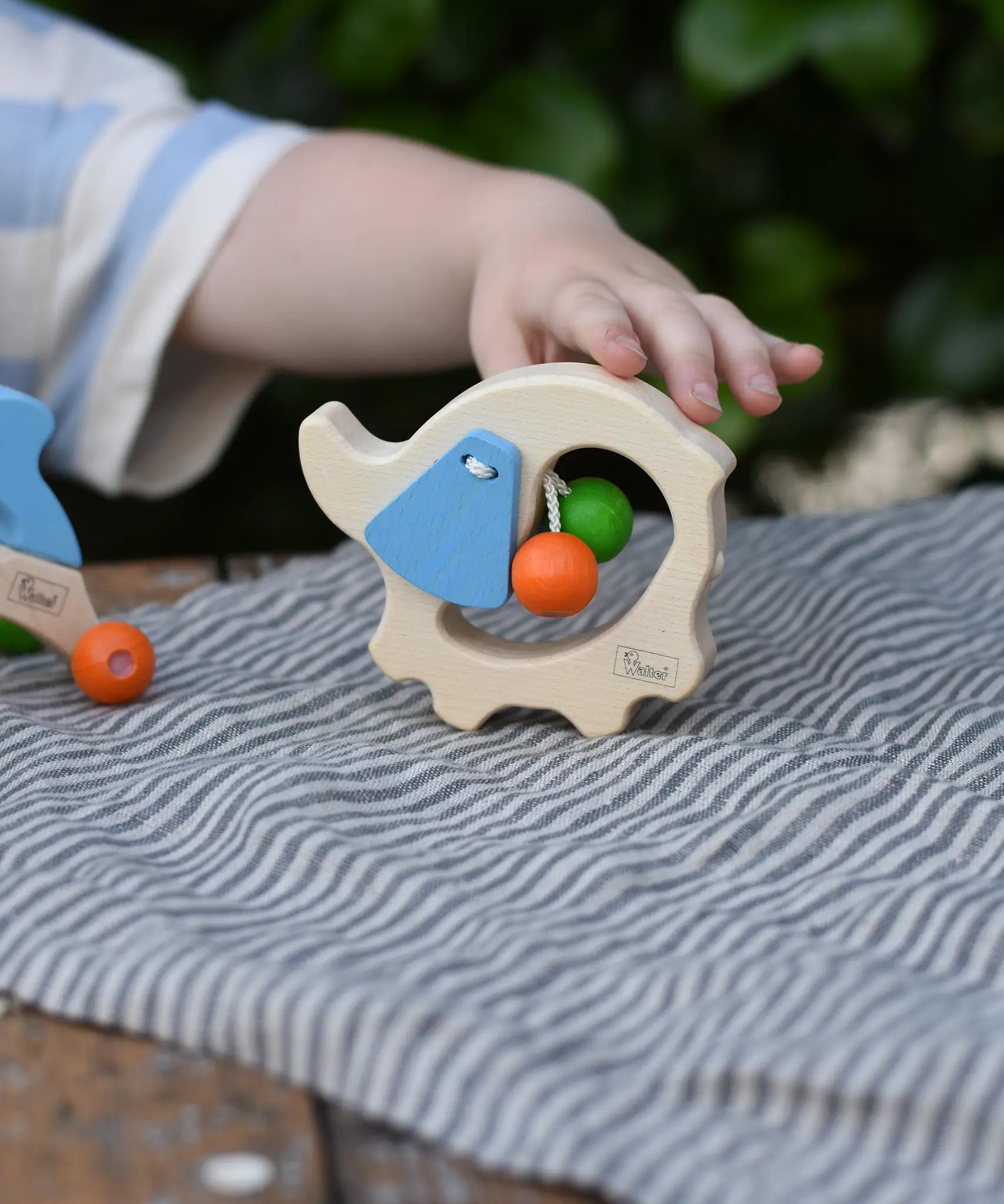 Child's hand reaching for the Nic elephant grasper wooden baby toy.